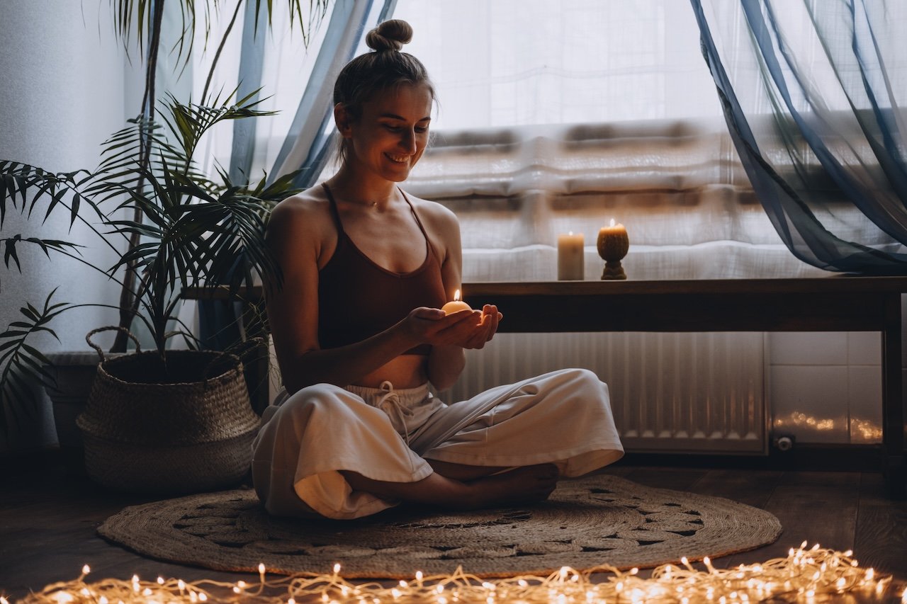 Young woman sitting on the floor, lights candles, enjoy meditation, do yoga exercise at home. Mental health, self care, No stress, healthy habit, mindfulness lifestyle, anxiety relief